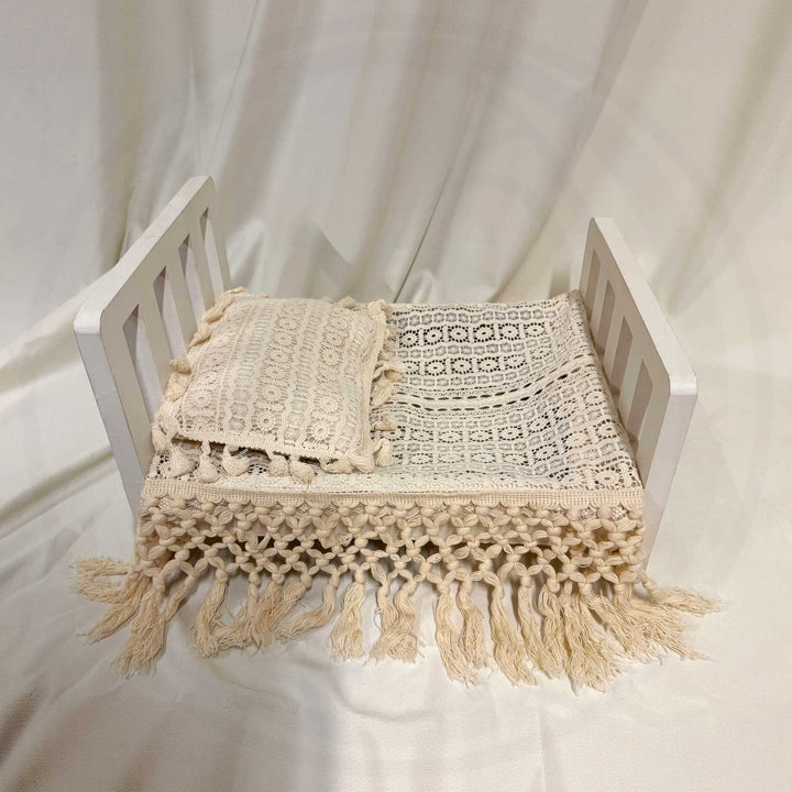 A beige cotton crochet set consisting of a rectangular blanket with a geometric openwork pattern and long knotted fringe, and a matching square pillow with floral motifs and tassels.
