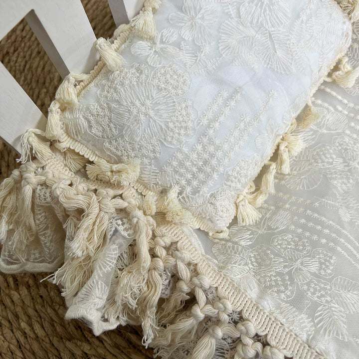 A close-up view of a beige floral embroidery lace pillow featuring ruffled tassel trim.