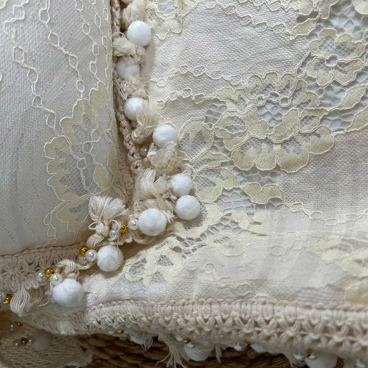 A close-up view of a beige lace textile featuring ruffled edges and pearl trim.