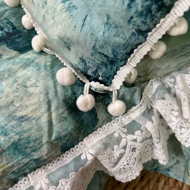 A close-up view of a blue tie dye pillow featuring ruffled pom-pom trim.