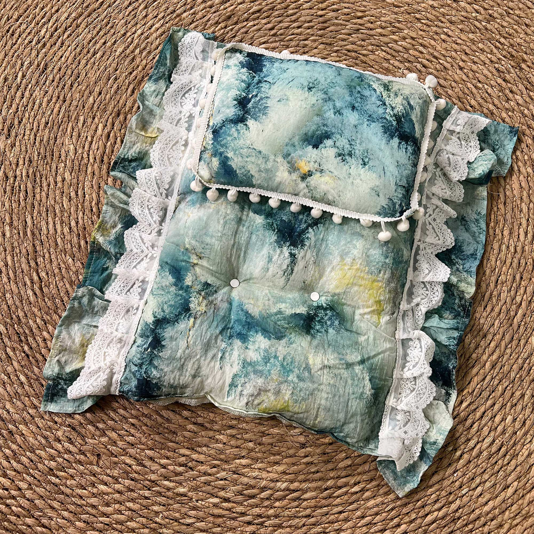 A 2-piece set featuring a newborn blanket and pillow with blue tie-dye and pom pom trim for newborn photography.