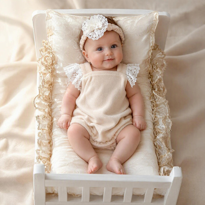 The newborn wears a polar fleece romper featuring white lace ruffled short sleeves attached at the shoulders and wears a pleated headband with flower.