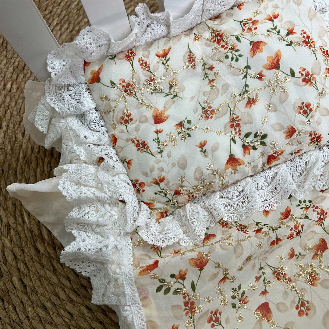 A close-up view of an orange floral print pillow featuring ruffled lace trim.