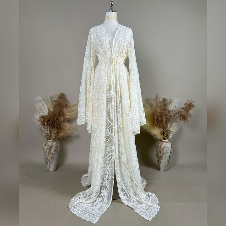 A beige lace ,Abrota dress with long bell sleeves and a V-neckline, displayed on a mannequin. The robe features a tie waist, an open front, and a floor-length train with scalloped edges.