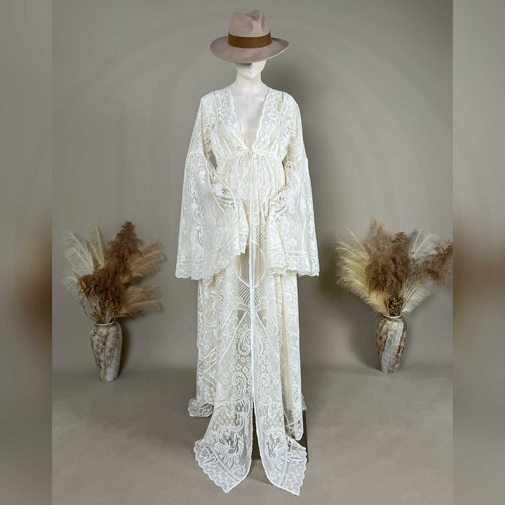 A beige lace ,Abrota dress with long bell sleeves and a V-neckline, displayed on a mannequin. The robe features a tie waist, an open front, and a floor-length train with scalloped edges.