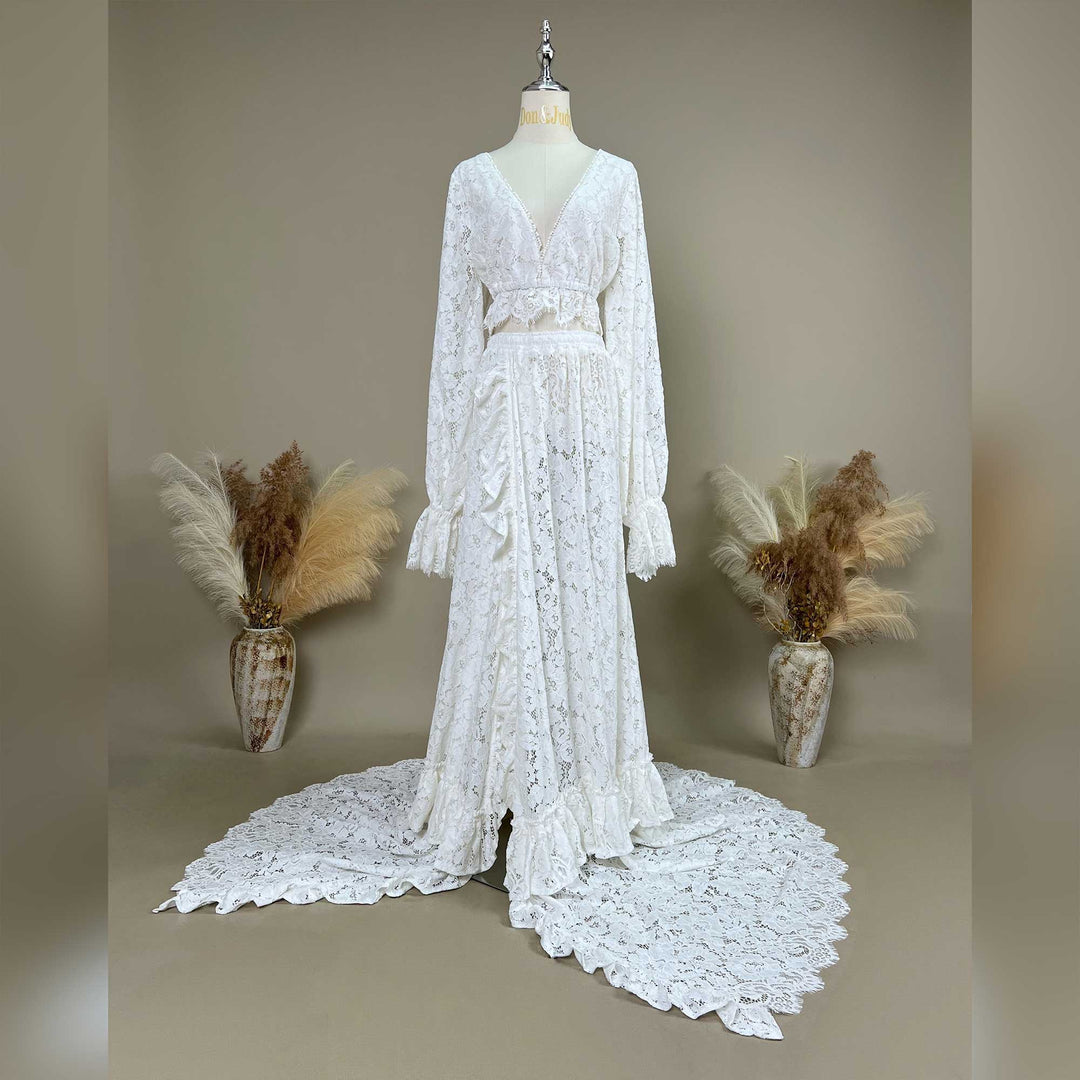 A ivory lace gown is displayed on a mannequin with dried flowers on both sides; the dress features a V-neck, long sleeves, a train, and a waist cutout.