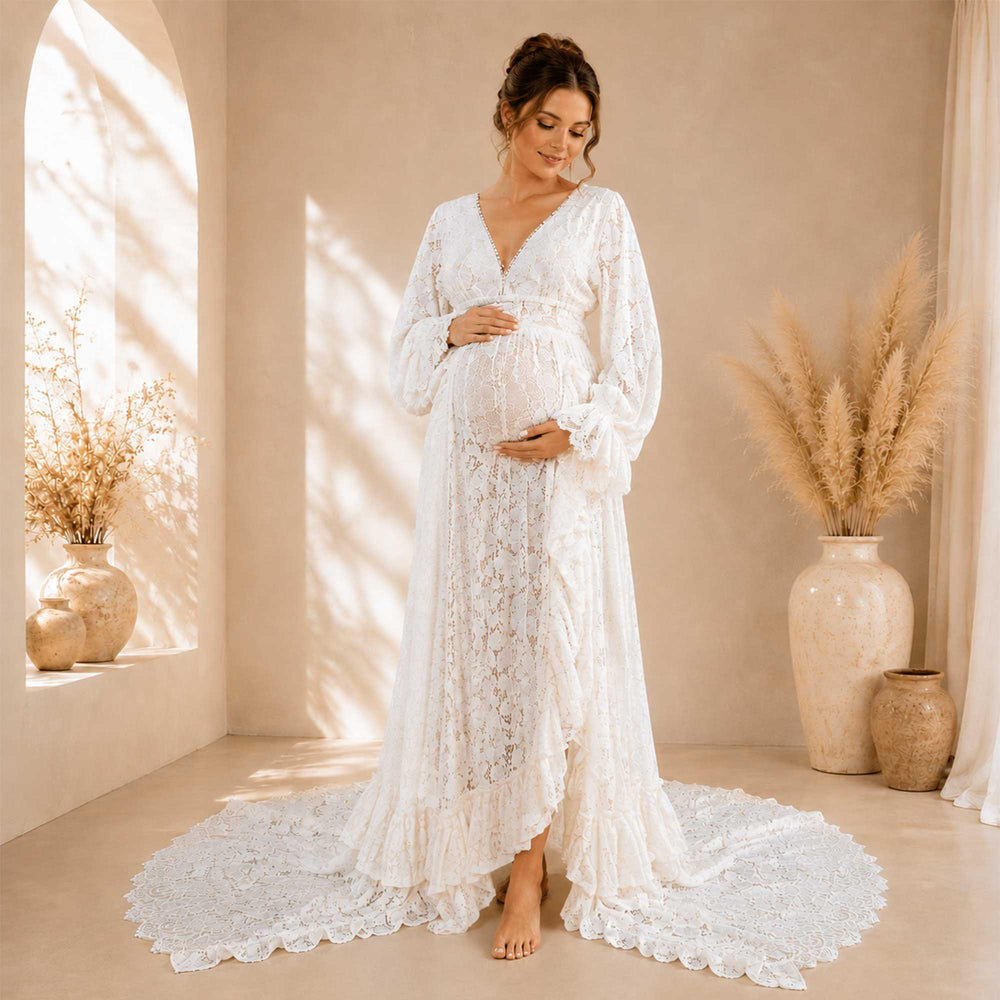 A pregnant woman wears the ivory lace gown standing before an indoor arch, cradling her belly.