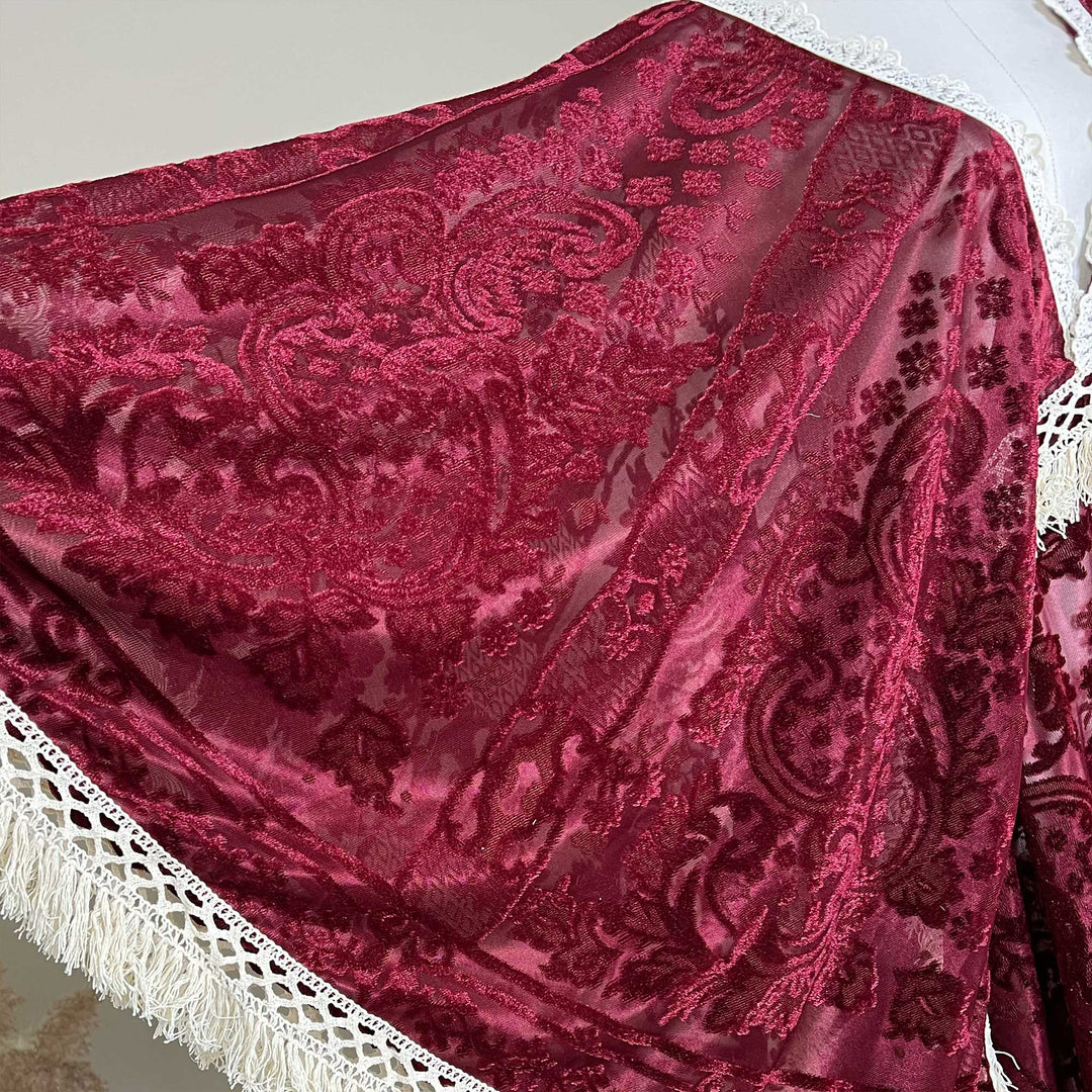 A close-up of a deep magenta velvet shawl with intricate floral embroidery and a white trim with fringe, draped on a white mannequin torso.