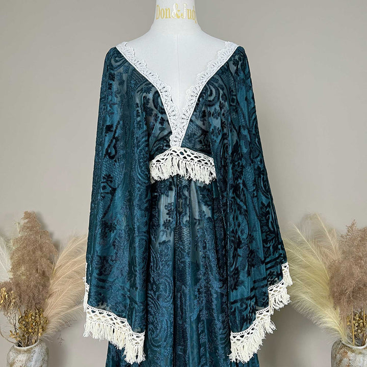 A green with white crochet trim and fringe, displayed on a white mannequin torso against a neutral beige background with dried pampas grass decor.