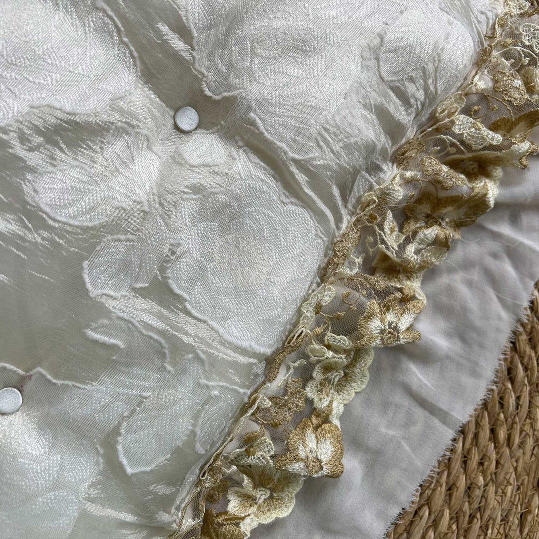 A close-up view of a beige floral pillow featuring ruffled lace trim.