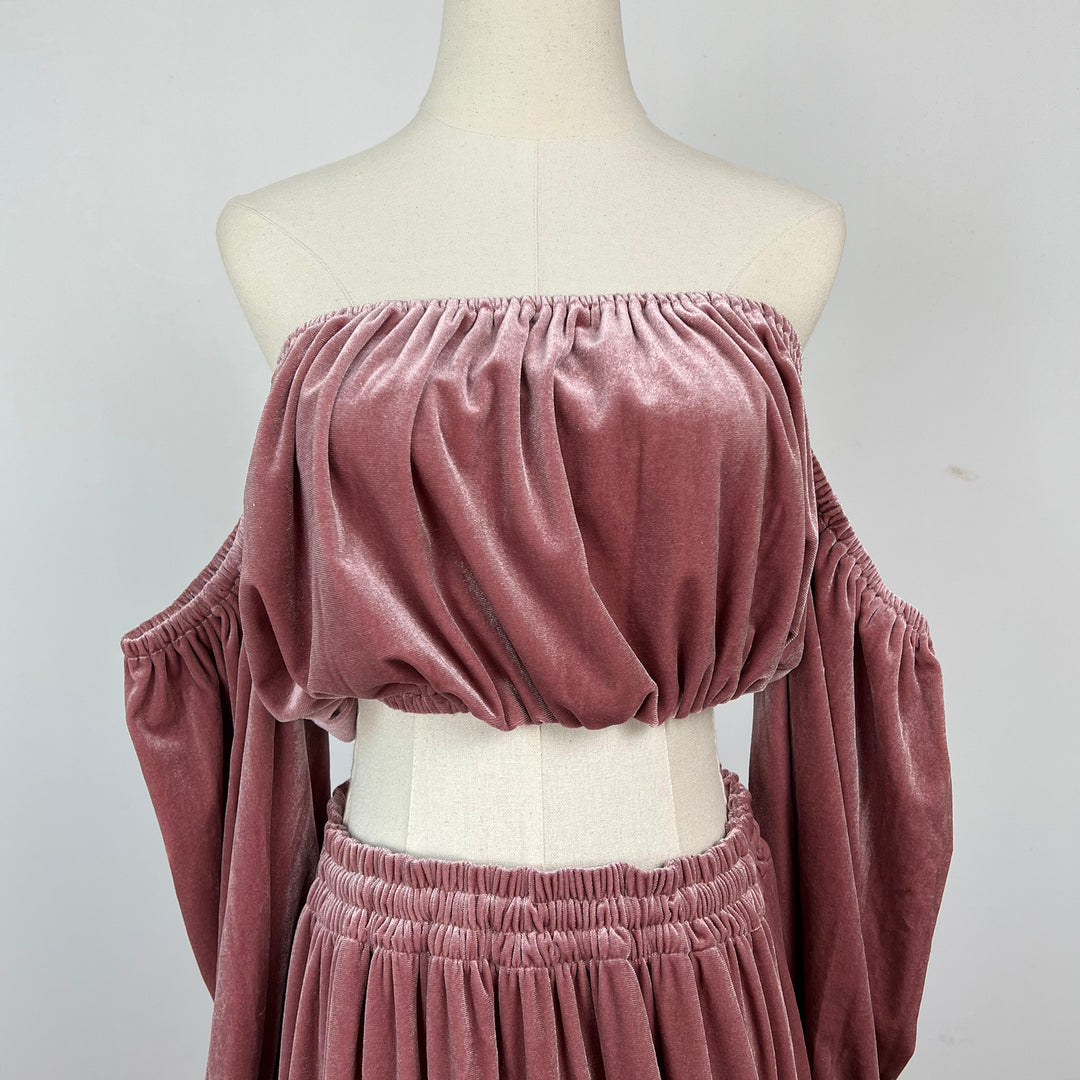 A dusty rose velvet two-piece set displayed on a cream mannequin torso. The set includes an off-the-shoulder, gathered bust crop top with long draped sleeves, and a matching gathered skirt.