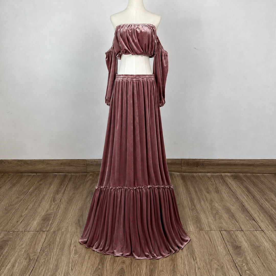 A dusty rose velvet two-piece set consisting of an off-the-shoulder long-sleeve crop top and a matching long pleated skirt, displayed on a mannequin against a neutral indoor wall and wood floor.