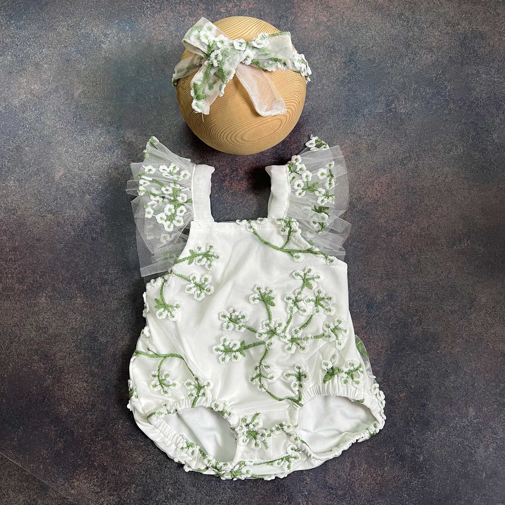 A romper laid flat from the front, showing the square neckline, tulle flower straps on both sides and gathered leg openings, with the same headband above.