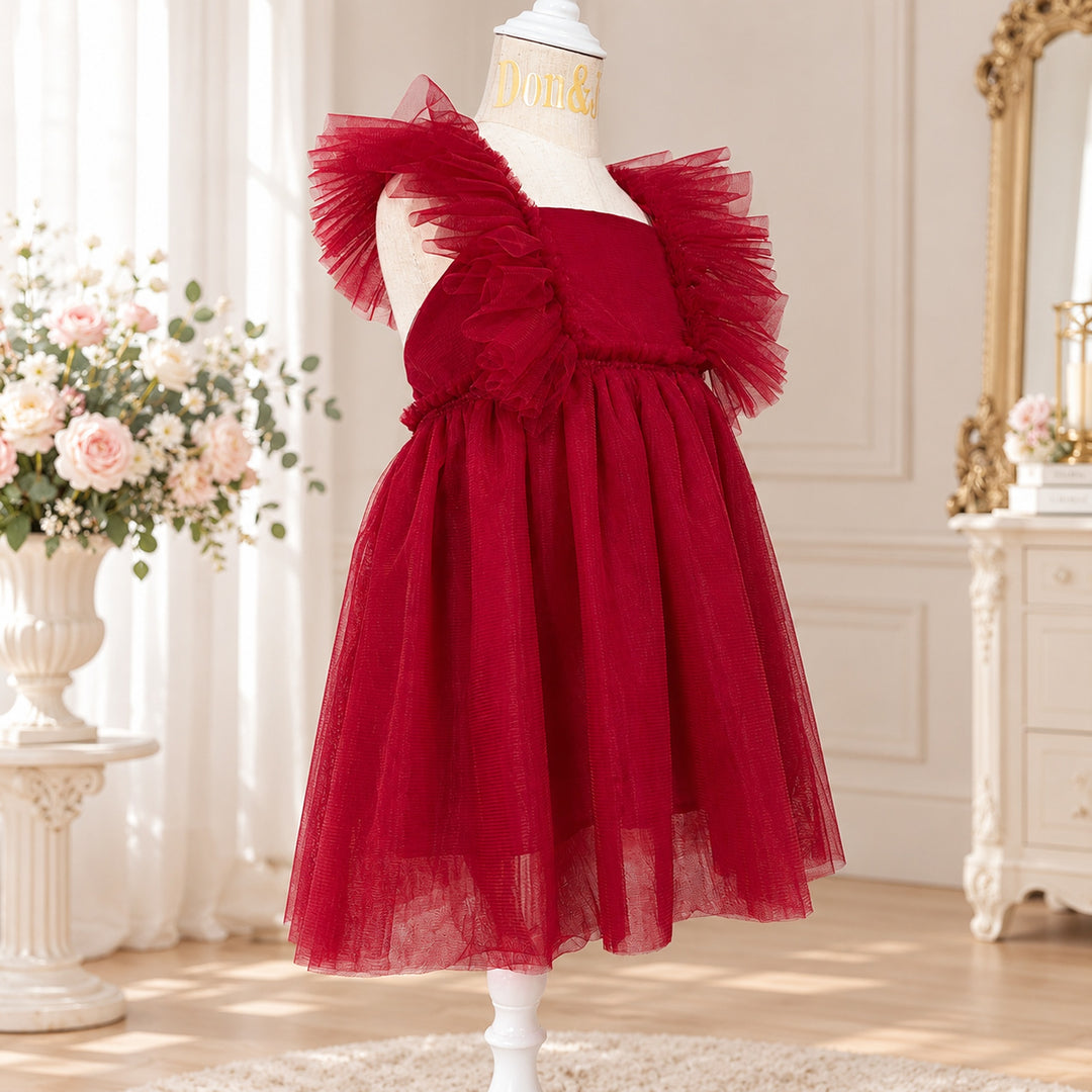 A Callisto red tulle dress on a mannequin with tulle ruffled shoulders; flowers and a mirror indoors.