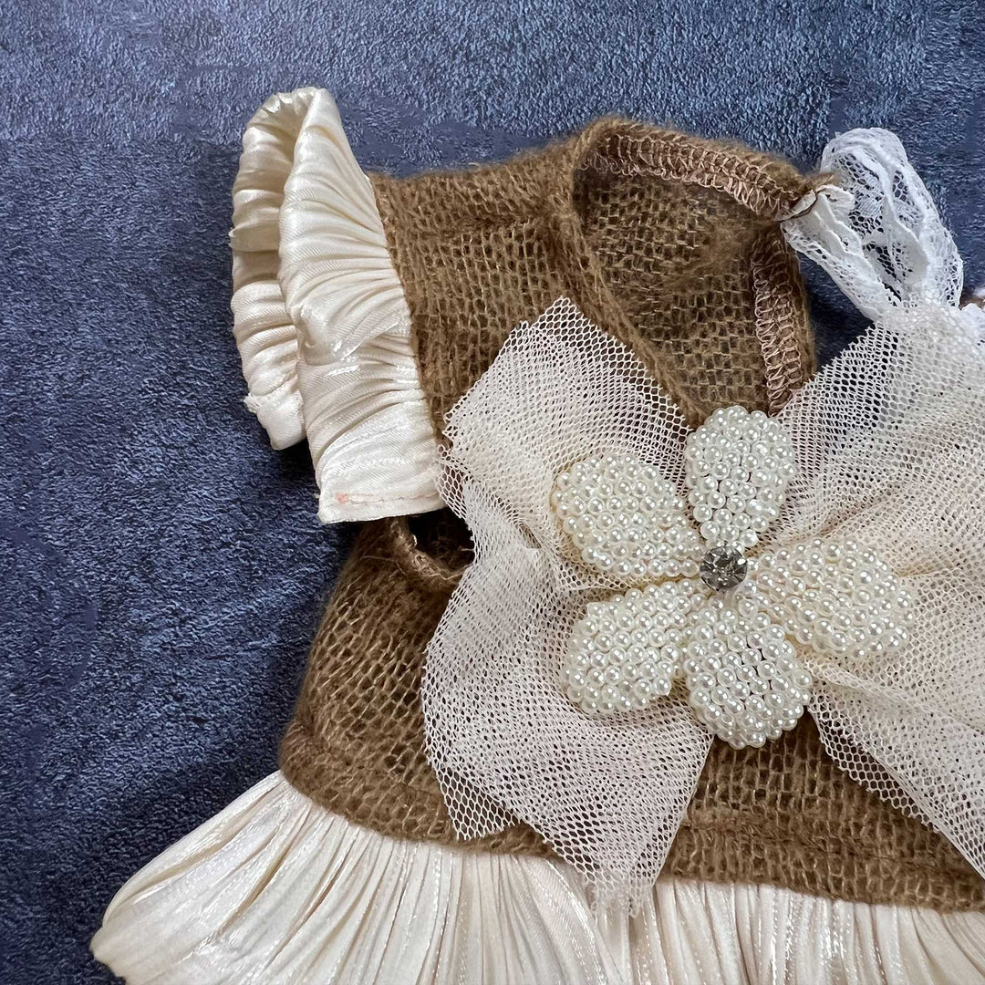Close-up shows camel mohair knit fabric, adorned with a mesh bow and pearl beaded flower, with pleated satin ruffled cuffs.