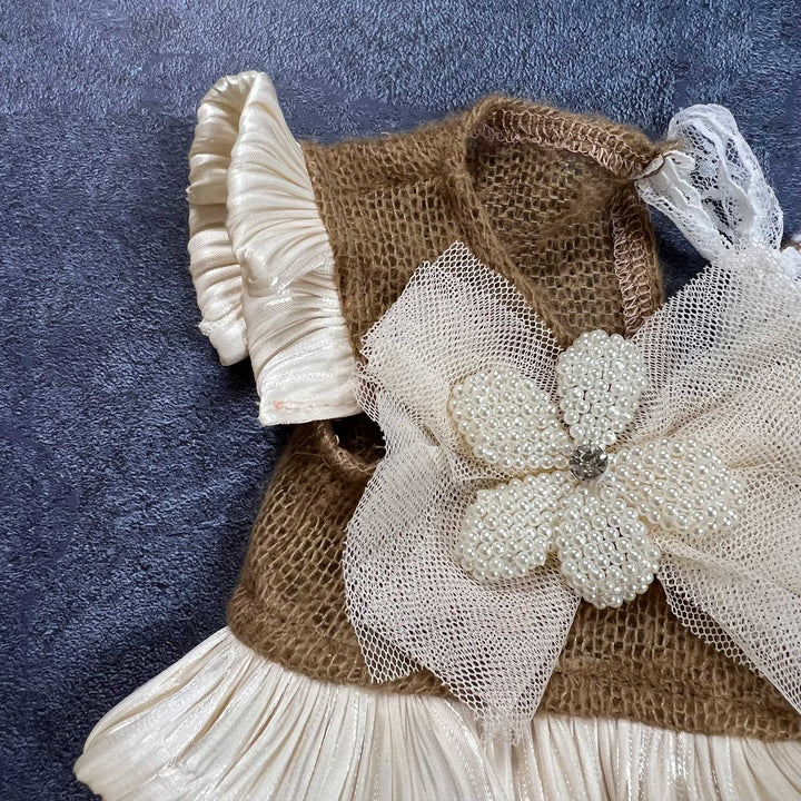 Close-up shows camel mohair knit fabric, adorned with a mesh bow and pearl beaded flower, with pleated satin ruffled cuffs.