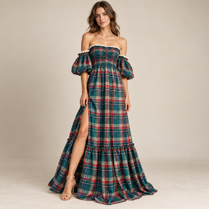 A woman in a Catubri green-red plaid off-shoulder maxi dress with puff sleeves, a side slit and a ruffled hem, wearing heeled sandals against a light backdrop.
