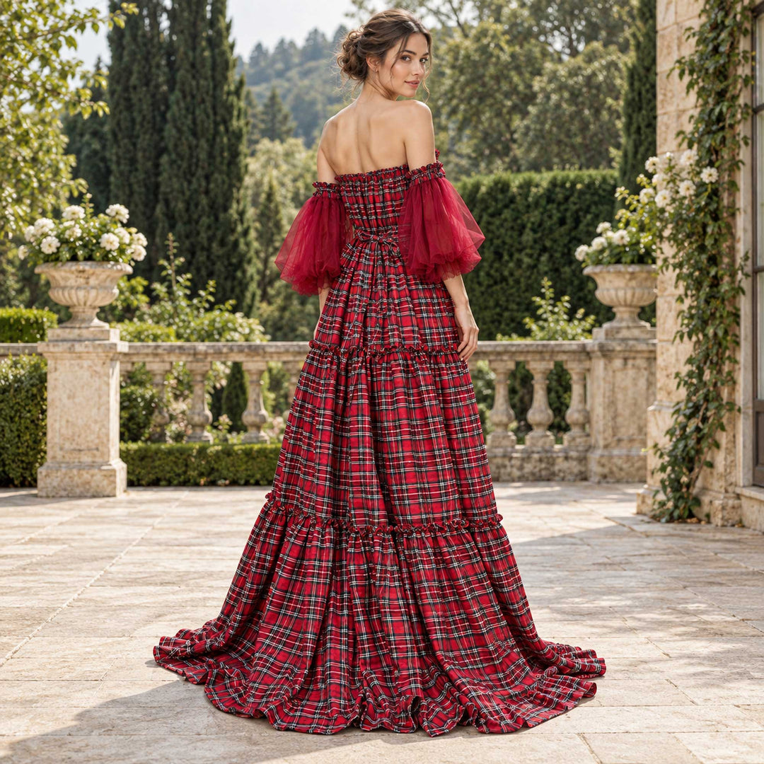 A woman seen from behind with her head turned, showing the Celaeno smocked back and tulle sleeves, on a stone terrace with a balustrade, planters and vines behind.