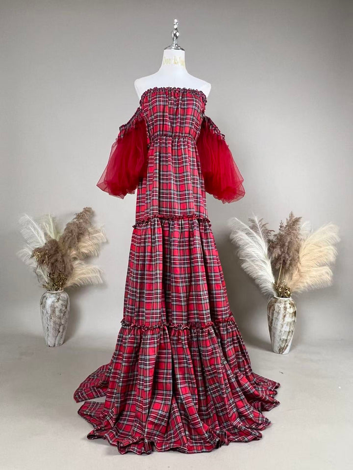 A Charybdis plaid off-shoulder dress with red tulle sleeves on a mannequin facing forward, tiered skirt, train on the floor, a dried-flower vase on each side.

