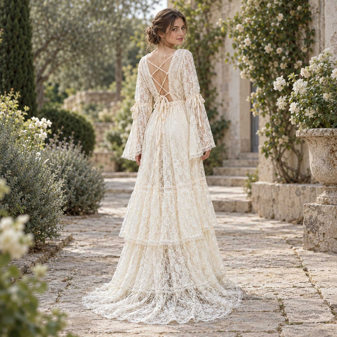 A woman seen from behind with her head turned, showing a Clito crisscross back straps and tied cuffs, on a stone path with shrubs and planters.