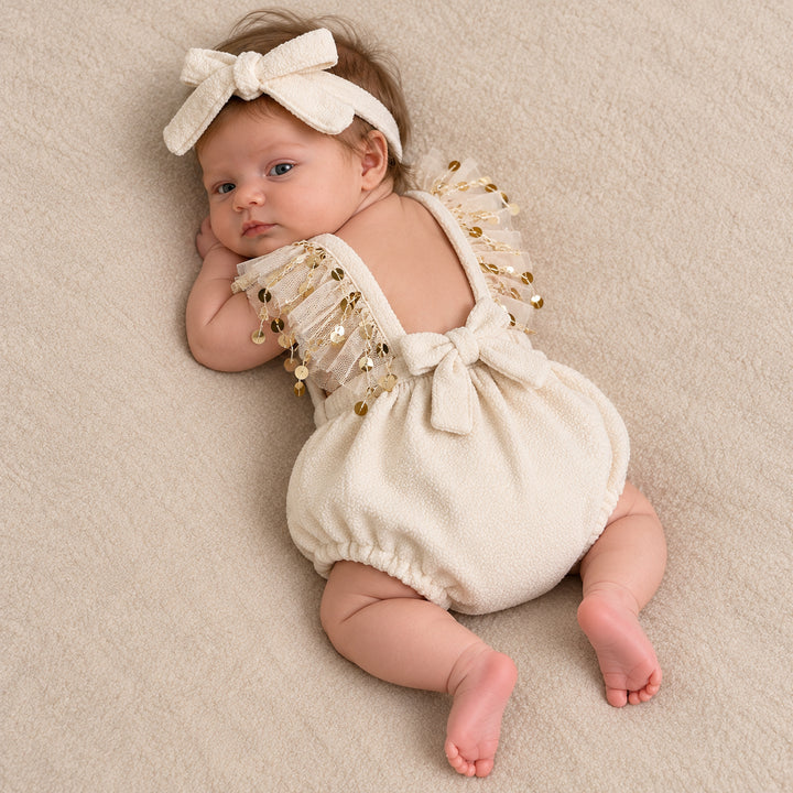 A baby lying on her side, showing the back bow tie and the tulle sequin straps, head turned toward the camera.