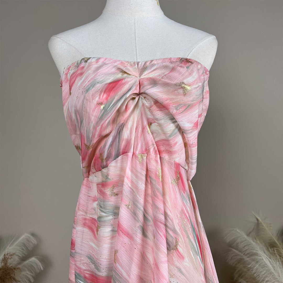 A close up of a pink printed strapless gown with pleats and a train.