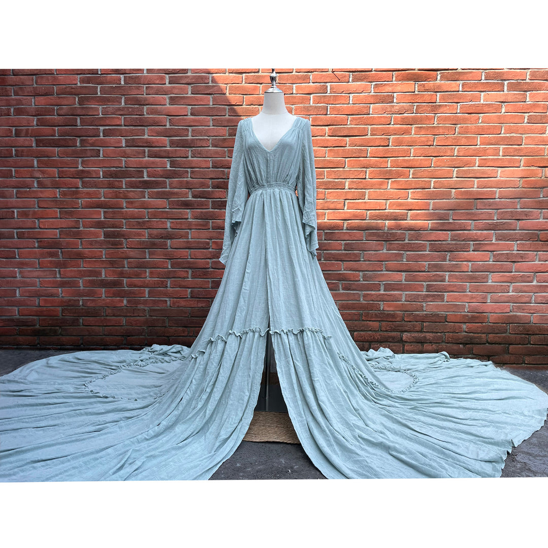 A light blue long-sleeved V-neck gown is displayed on a mannequin.The dress features a high front slit and its hem and train are spread out on the wooden floor.