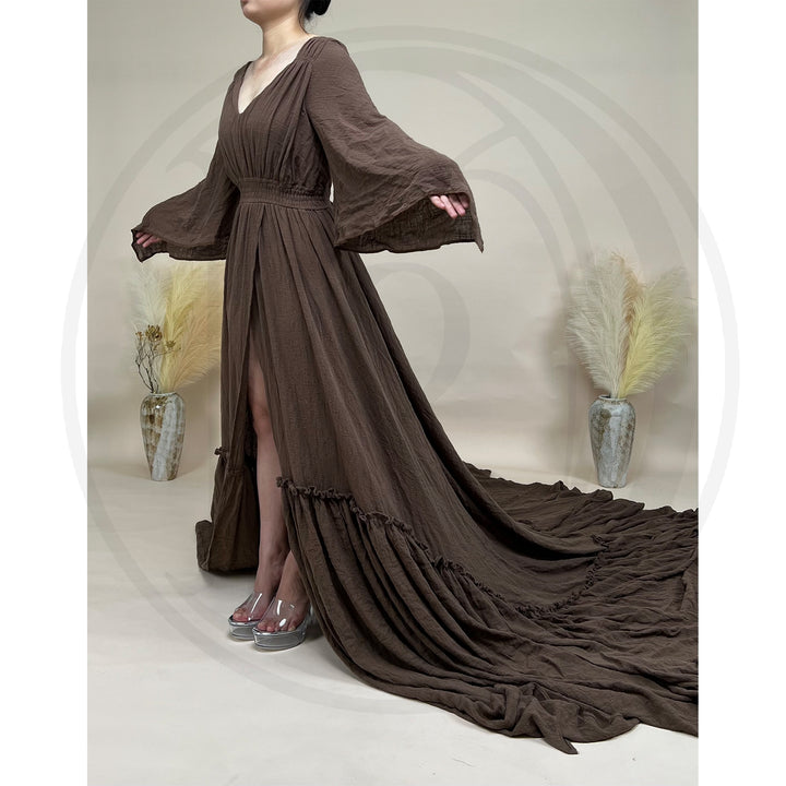 A Daphne coffee long-sleeved V-neck gown is displayed on a mannequin. The dress features a high front slit and its hem and train are spread out on the wooden floor.