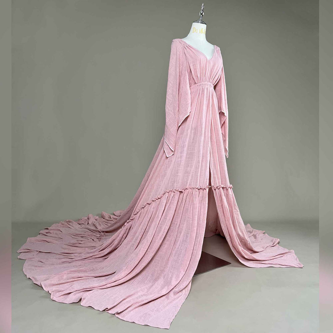 A Daphne Pink long-sleeved V-neck gown is displayed on a mannequin.The dress features a high front slit and its hem and train are spread out on the wooden floor.