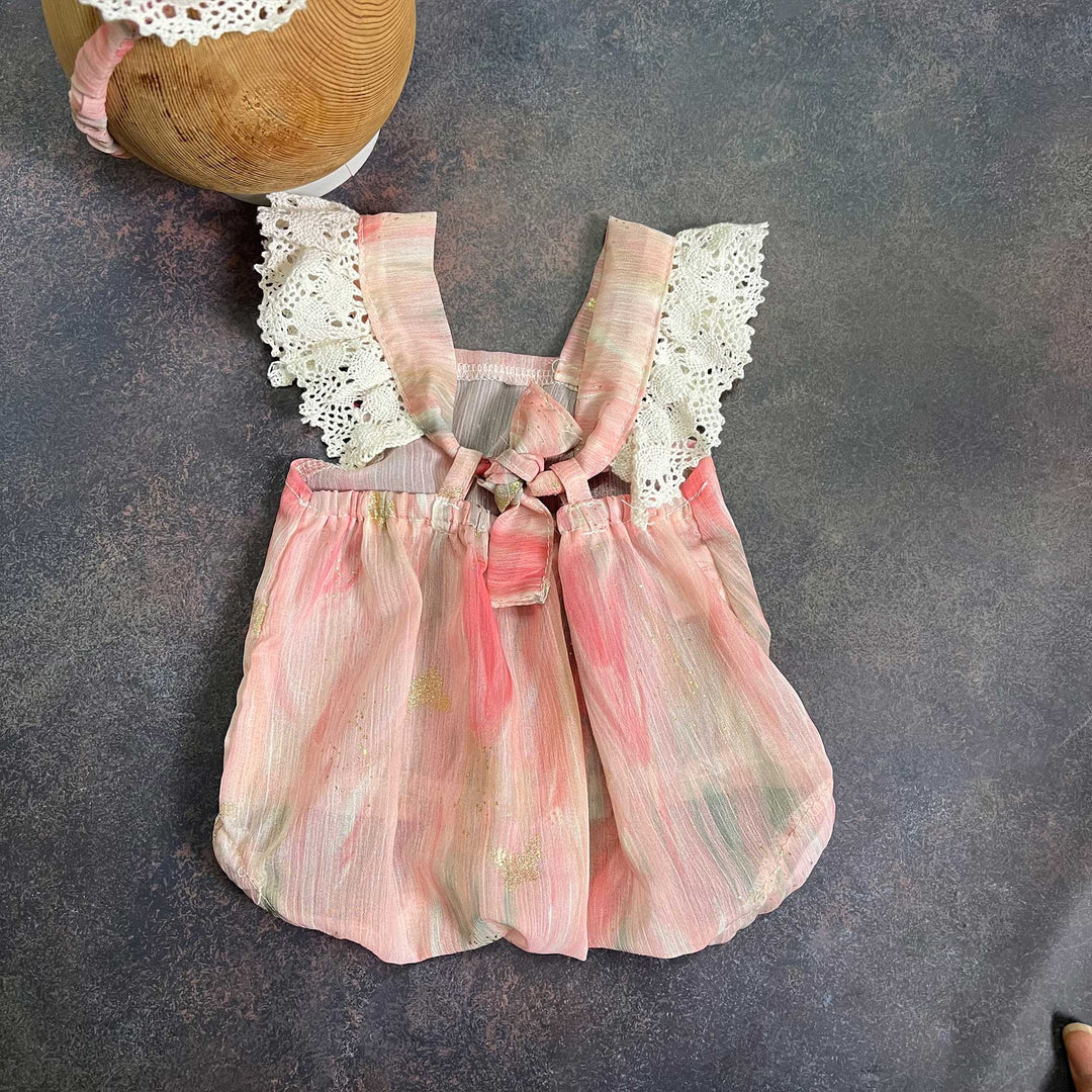 the back of a romper laid flat, straps tied at the chest, gathered waist, part of the headband visible at the upper left.