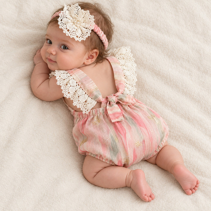 A baby lying on her side, showing the back strap bow and crochet lace, head turned toward the camera.