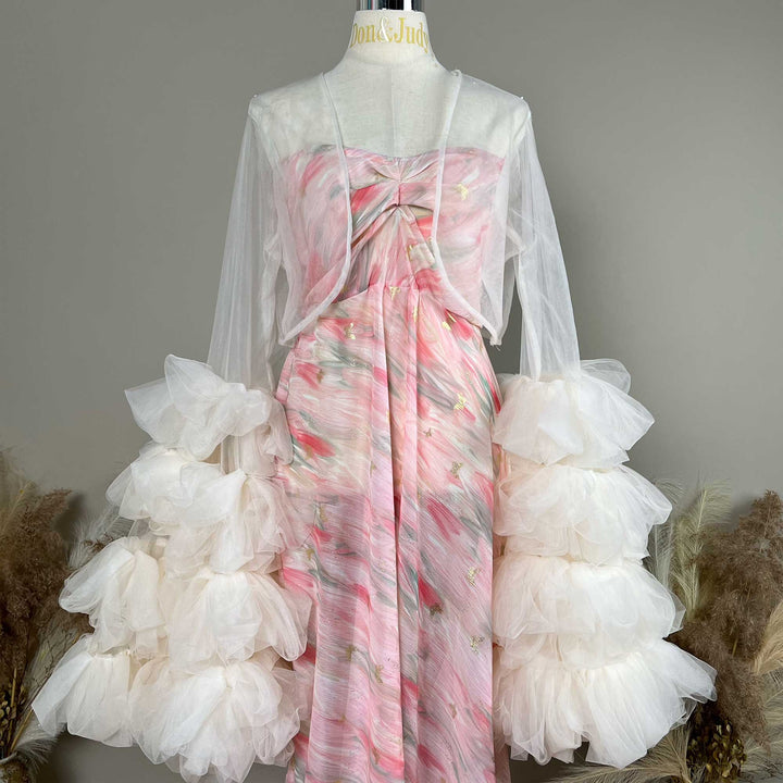 A mannequin displays a pink printed strapless dress with a light apricot  sheer bolero and tiered sleeves; the dress features pleats.