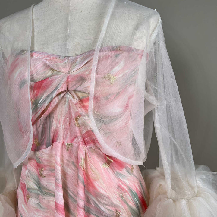 A close up of a pink printed strapless dress with a light apricot sheer bolero.