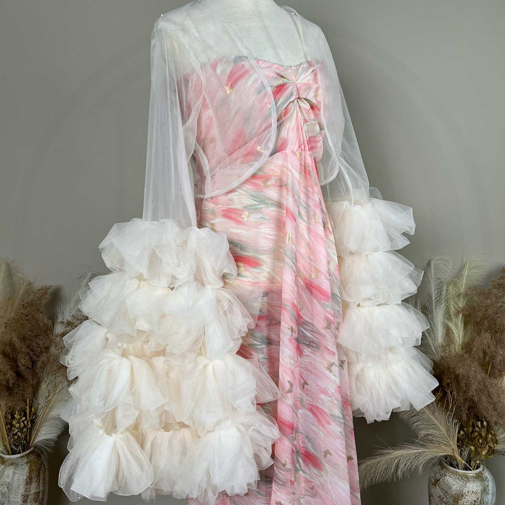 A mannequin displays a side view of a pink printed strapless dress with a light apricot sheer bolero and tiered sleeves; the dress features pleats.