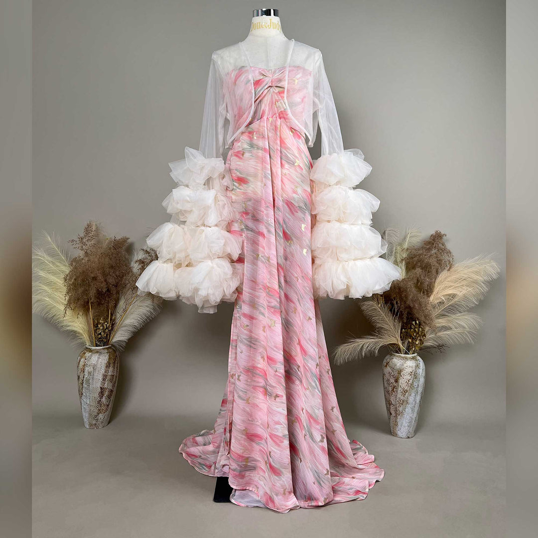 A mannequin displays a pink printed strapless gown with sheer white long sleeves and tiered cuffs; the dress features a train.