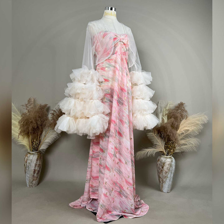 A mannequin displays a side view of a pink printed strapless gown with a light apricot sheer bolero and tiered cuffs; the dress features a train.