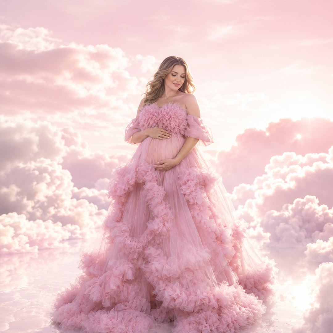 A pregnant woman stands in a pink off-shoulder ruffled gown, holding her belly; the dress features multi-layered ruffles.