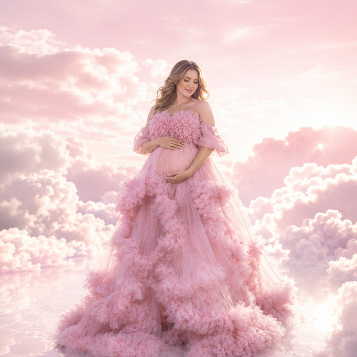 A pregnant woman stands in a pink off-shoulder ruffled gown, holding her belly; the dress features multi-layered ruffles.
