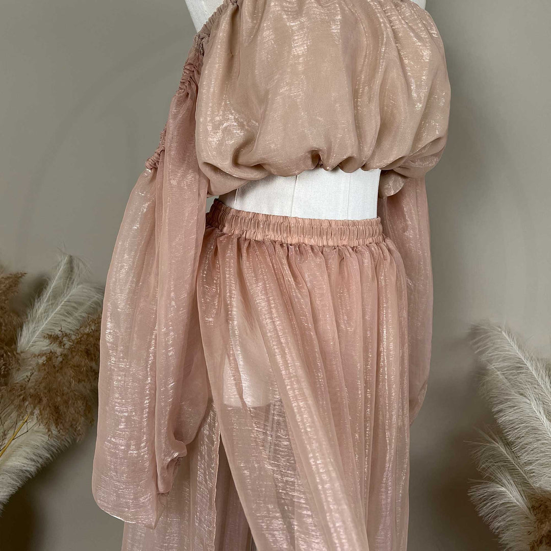 A mannequin displays a close-up of a two-piece maternity set featuring an off-shoulder top and elastic-waist tulle skirt; the fabric has a sheen.
