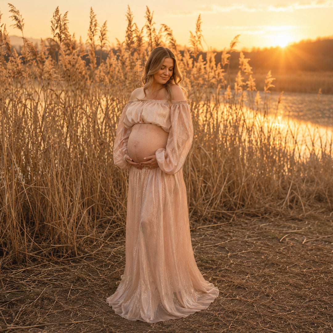 A pregnant woman stands in reeds wearing a off-shoulder sequin gown, holding her belly; the dress features lantern sleeves and a floor-length skirt.
