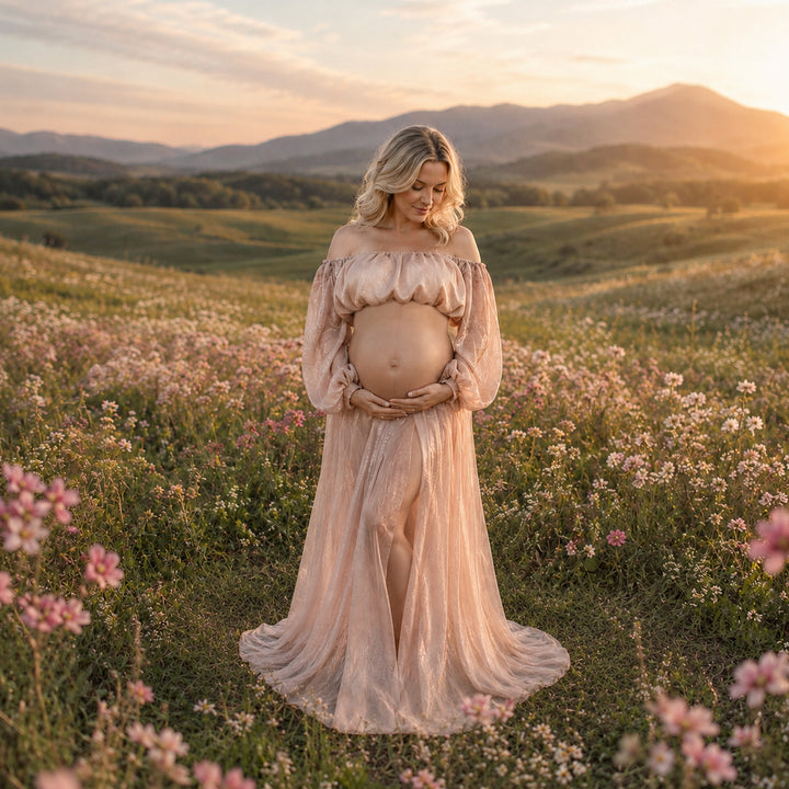 A pregnant woman stands in a flower field wearing a off-shoulder chiffon gown, holding her belly; the dress features lantern sleeves and a front slit.