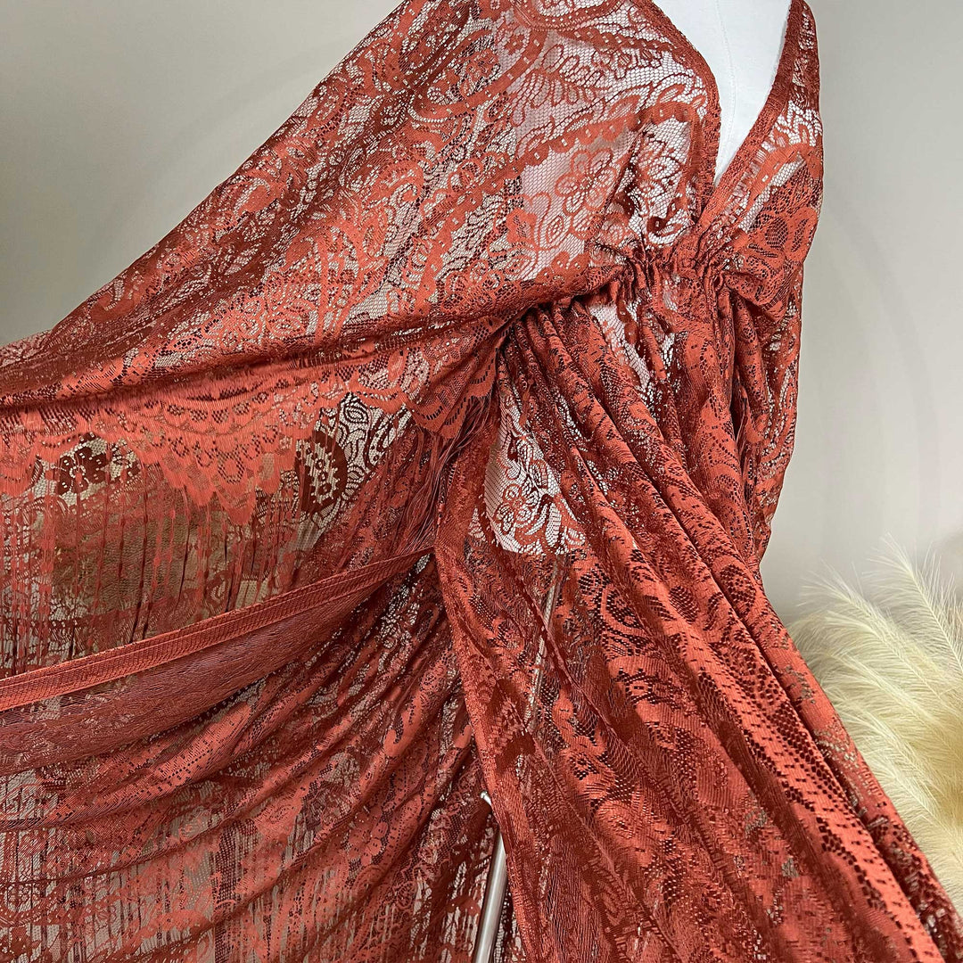 A mannequin displays a close-up of a rust lace cape featuring floral openwork texture and a deep V-neck; the fabric is semi-transparent mesh.
