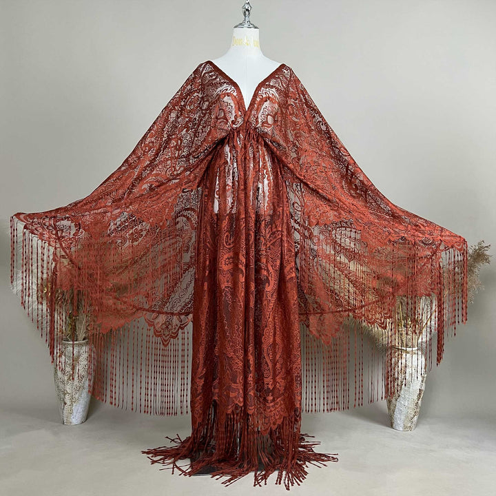 A mannequin displays a rust lace fringe cape with a deep V-neck and wide sleeves; the fabric features an openwork pattern.