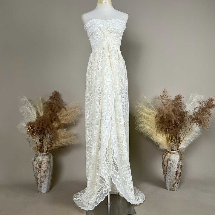 A mannequin displays a beige strapless lace gown with a ruched bodice and train; the dress features an openwork pattern.