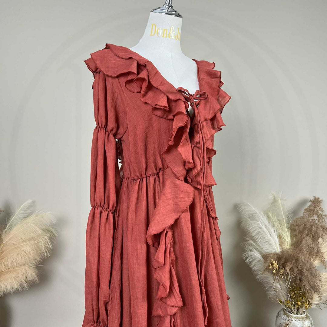 A terracotta-colored linen Kallectoria dress with dramatic ruffles and long sleeves, displayed on a white mannequin torso. The dress features a tie-front neckline and gathered waist details.