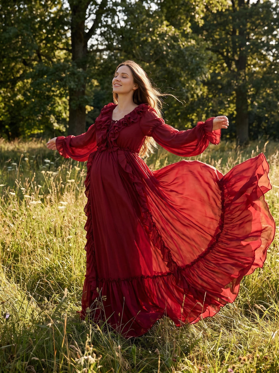 A pregnant woman in a red Kallectoria dress stands in a grassy field with her arms outstretched, and the skirt billows out. The background consists of trees and plants.