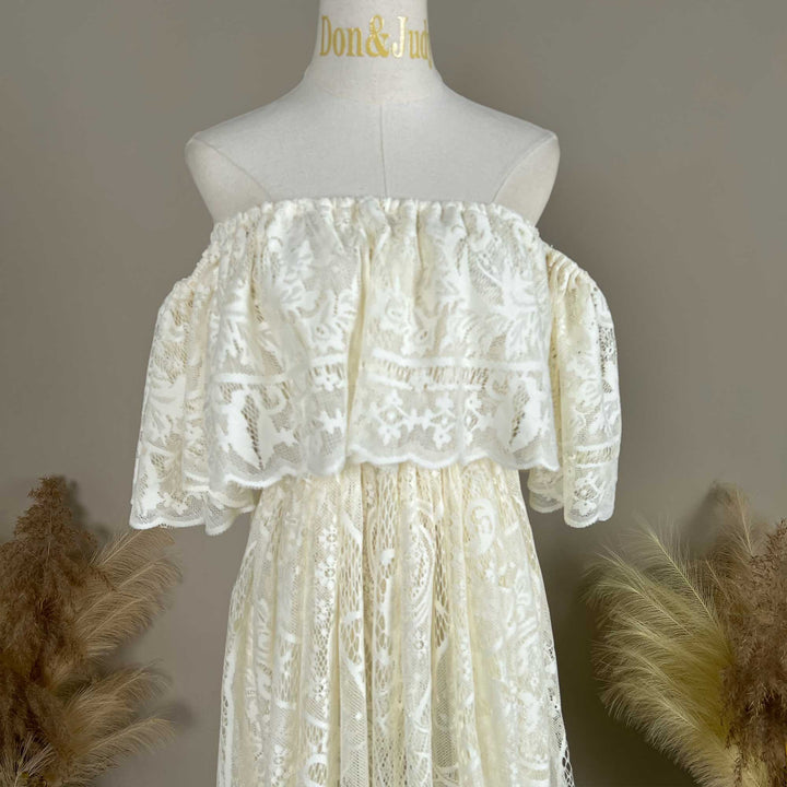 A mannequin displays the upper body of a beige off-shoulder lace gown with ruffled sleeves and a train.