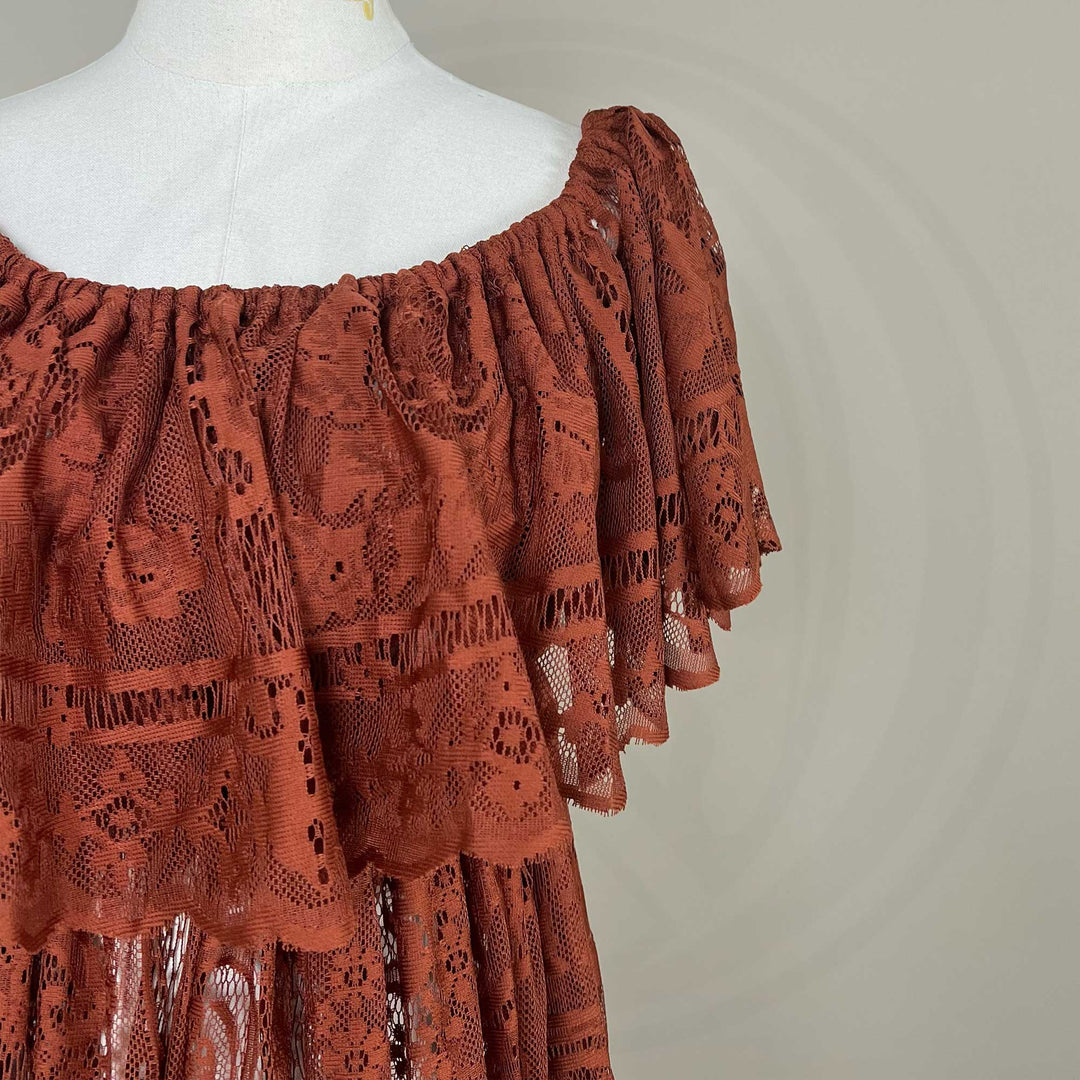 A mannequin displays a close-up of a terracotta off-shoulder lace dress with a ruched neckline and tiered sleeves; the fabric features an openwork pattern.
