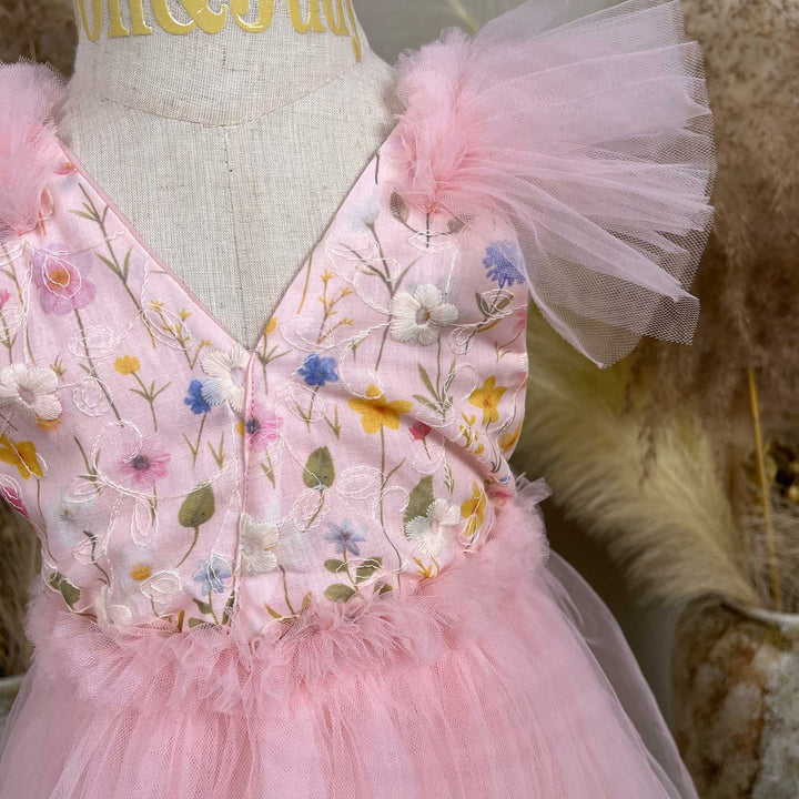 A mannequin displays a close-up of a pink V-neck dress with colorful floral embroidery and tulle sleeves; the waist features tulle ruffles.