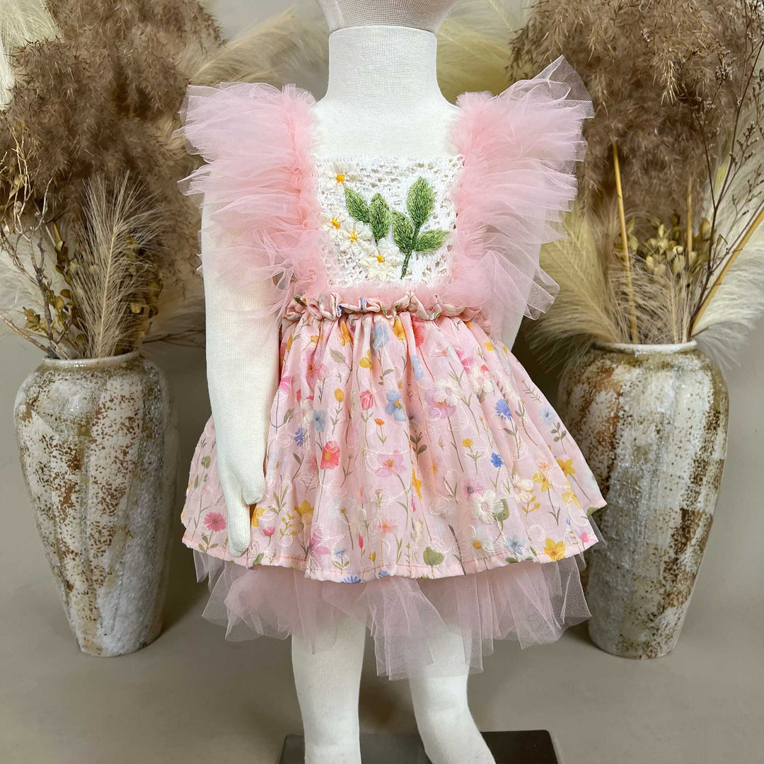 A mannequin displays a pink floral dress with a crochet bodice, green leaf embroidery, and tulle sleeves; the skirt features layered tulle.